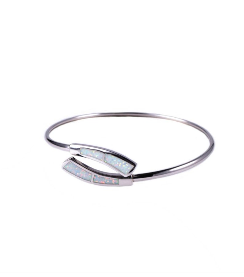 May include: A silver bangle bracelet with a white opal design. The bracelet is open and has a simple, elegant design.