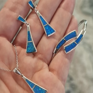 May include: A silver necklace, earrings, and bracelet set with blue opal stones. The jewelry is in the shape of a triangle.