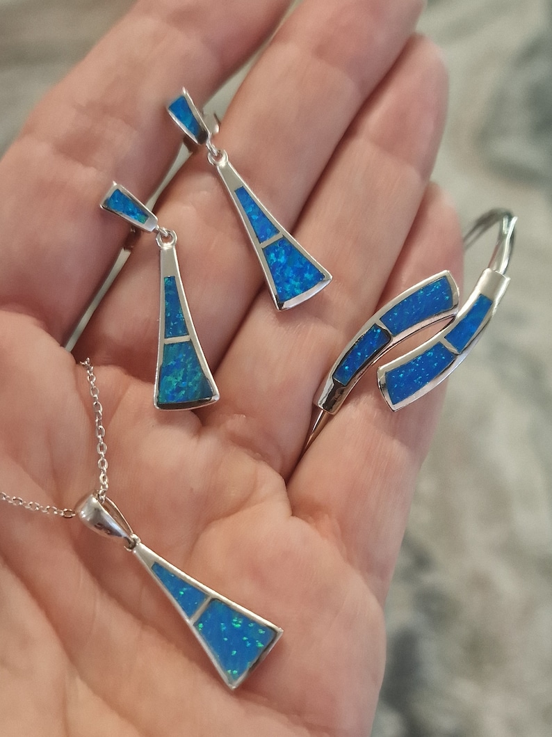 May include: A silver necklace, earrings, and bracelet set with blue opal stones. The jewelry is in the shape of a triangle.