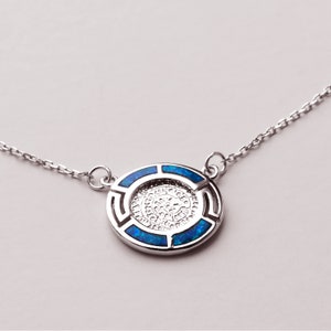 May include: A silver necklace with a round pendant featuring a blue opal inlay. The pendant has a geometric design around the edge.