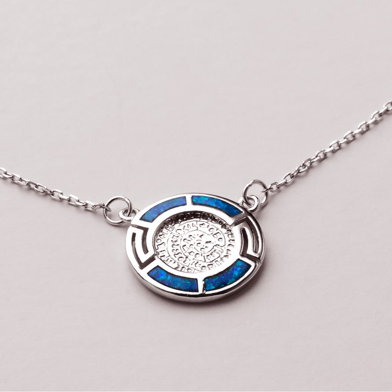 May include: A silver necklace with a round pendant featuring a blue opal inlay. The pendant has a geometric design around the edge.