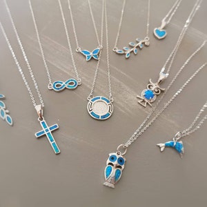 May include: A collection of silver necklaces with blue opal pendants. The pendants include a cross, an owl, a butterfly, an infinity symbol, a leaf, a circle, a dolphin, and a heart.