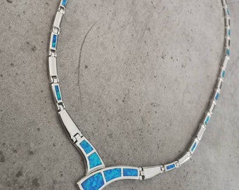 May include: A silver necklace with a blue opal pendant. The pendant is shaped like a V and has a row of blue opals on each side.