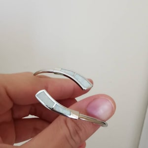 May include: A silver bangle bracelet with two white opal inlays.