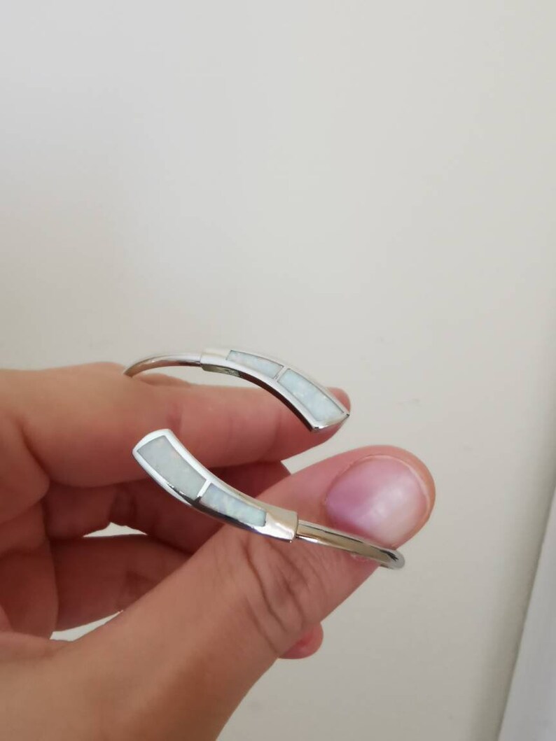 May include: A silver bangle bracelet with two white opal inlays.