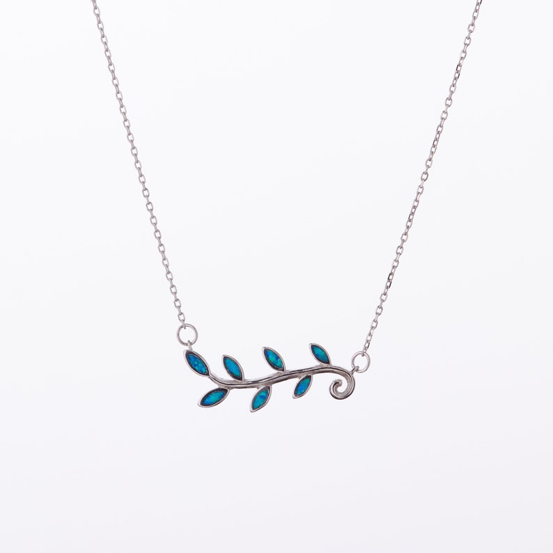 May include: A silver necklace with a delicate branch design featuring blue opal leaves. The branch has a curled end and is set on a silver chain.