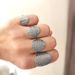 May include: Four silver rings with a circular design featuring intricate patterns and symbols. The rings are worn on a hand.