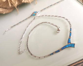May include: A silver necklace with a blue opal pendant. The necklace has a delicate chain and a V-shaped pendant with a blue opal stone.