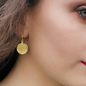 May include: A pair of gold dangle earrings with a round, textured disc pendant.