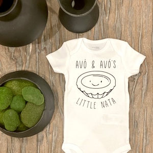 May include: White baby onesie with black text that reads "Avô & Avós Little Nata" and a cartoon drawing of a Portuguese custard tart with a smiling face.
