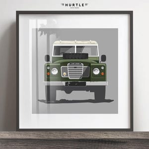 Op de afbeelding: Een groene Land Rover Defender met een wit dak en een grijze achtergrond. De auto is naar de camera gericht en de grille is zichtbaar. De tekst "LAND ROVER" is zichtbaar op de grille.