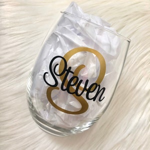 May include: A clear glass wine glass with a gold and black vinyl decal that says "Steven".
