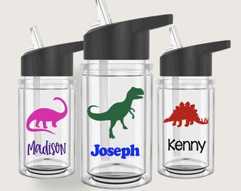 May include: Three clear plastic water bottles with black lids and straws. Each bottle has a different dinosaur silhouette and a name printed on the front: Madison, Joseph, and Kenny.
