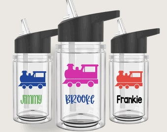 May include: Three clear plastic water bottles with black lids and straws. Each bottle has a train design and a name on the front: Jimmy, Brooke, and Frankie.