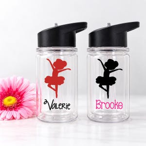 May include: Two clear plastic water bottles with black lids and straws. One bottle features a red ballerina silhouette and the name Valerie in black. The other bottle features a black ballerina silhouette and the name Brooke in pink.