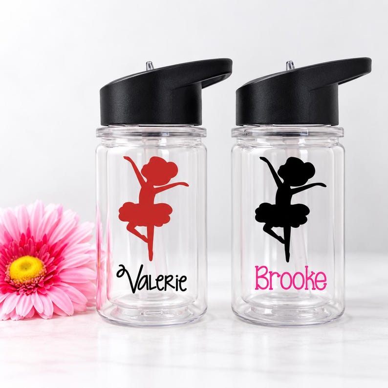 May include: Two clear plastic water bottles with black lids and straws. One bottle features a red ballerina silhouette and the name Valerie in black. The other bottle features a black ballerina silhouette and the name Brooke in pink.