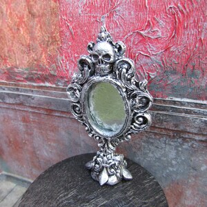May include: Silver ornate tabletop mirror with a skull design and a beveled glass surface.