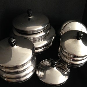 May include: A set of six silver-colored metal serving bowls with black handles. The bowls are stacked in pairs, with the largest bowl on top.