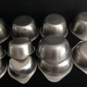 May include: A set of nine stainless steel mixing bowls, some with a smooth finish and others with a perforated bottom.