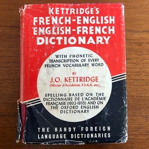 May include: A red and black book titled "Kettrdige's French-English English-French Dictionary" with phonetic transcription of every French vocabulary word by J.O. Kettrdige, Officier d'Academie, F.S.A.A. etc. The book is part of "The Handy Foreign Language Dictionaries" series.