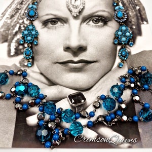 Puede incluir: Un collar de cadena de plata con cuentas azules y plateadas. El collar está drapeado sobre las manos de una mujer, y la imagen está en blanco y negro. El texto "CrimsonQueens" es visible en la parte inferior de la imagen.