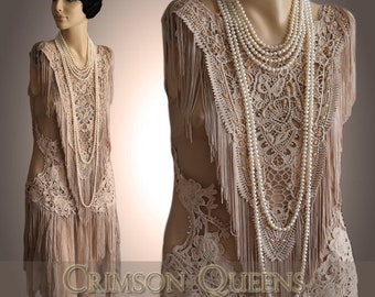 May include: A beige flapper dress with fringe and lace detailing. The dress is paired with a long pearl necklace.