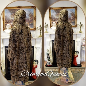 May include: A long, hooded coat with a textured, mottled pattern in shades of brown and black. The coat is displayed in front of a fireplace with decorative elements. The text "Crimson Queens" is visible at the bottom.