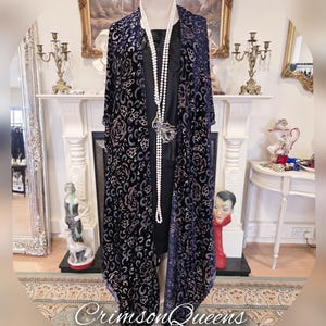 May include: A long, navy blue velvet shawl with a floral pattern in shades of pink and cream. The shawl is draped over a mannequin and has a fringed edge.