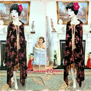 May include: A black velvet shawl with a floral pattern in shades of pink and gold. The shawl is draped over a mannequin wearing a gold dress and a pearl necklace. The shawl has a long, flowing design and is perfect for adding a touch of elegance to any outfit.