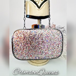 Op de afbeelding: Een zilveren clutch met een kettingband. De tas is bedekt met kleurrijk glitter.