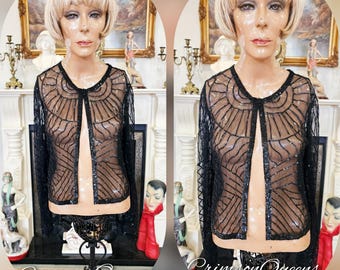 May include: A black beaded cardigan with a geometric pattern. The cardigan is open in the front and has long sleeves.