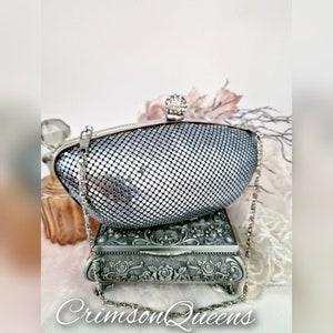 May include: A silver mesh clutch purse with a silver chain strap and a rhinestone embellishment on the clasp.