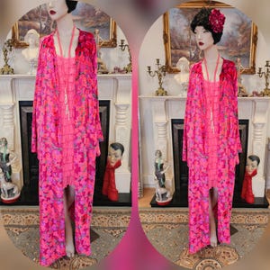 Könnte beinhalten: Eine rosa Samt-Robe mit floralem Muster und einer langen, fließenden Silhouette. Die Robe hat einen Schalkragen und lange Ärmel. Das Model trägt unter der Robe ein rosa Kleid.