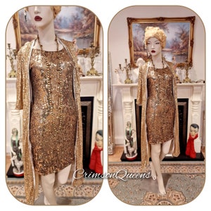 May include: A gold sequined dress with a matching long-sleeved jacket. The dress has a scoop neckline and a fitted silhouette. The jacket has a shawl collar and a flowing silhouette. The dress and jacket are displayed on a mannequin.