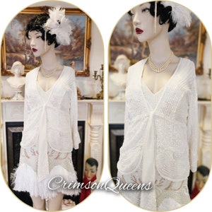 Peut inclure: Une robe de flapper blanche à paillettes avec une veste assortie. La robe a une frange sur le bas et un motif à paillettes. La veste a un col en V et une cravate à la taille.