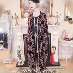 Puede incluir: Un chal largo de terciopelo burdeos con un patrón de paisley. El chal está drapeado sobre un maniquí que lleva un vestido negro y un collar de perlas. El maniquí lleva una diadema negra con un diseño floral.