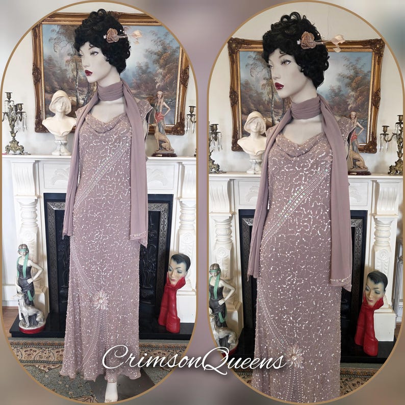 May include: A mauve, floor-length gown with detailed beadwork and a cowl neckline. The dress is accompanied by a matching scarf. The mannequin wears a black wig with a flower. The text "Crimson Queens" is visible.