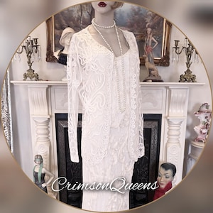 Puede incluir: Un vestido de encaje blanco con una chaqueta a juego de manga larga y un collar de perlas. El vestido y la chaqueta presentan intrincados diseños florales. La imagen está enmarcada y contiene el texto "Crimson Queens".