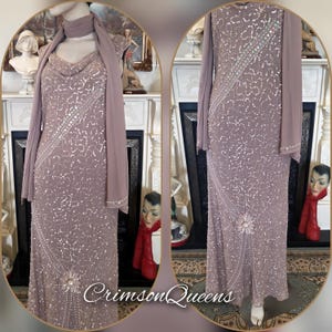 May include: A mauve, floor-length gown with a cowl neckline and long sleeves. The dress is adorned with sequins and beads in a floral design. A matching scarf is draped over the shoulders. The text "Crimson Queens" is visible at the bottom.