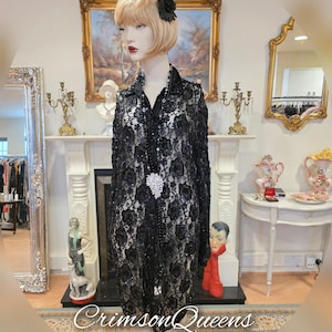 May include: A black sequined and beaded lace dress with a long sleeve and a collared neckline. The dress has a floral pattern and a jeweled brooch.