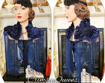 May include: A navy blue vintage style cape with a ruffled collar and a black velvet ribbon tie. The cape is displayed on a mannequin with a black headband and a jeweled necklace.