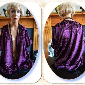 May include: A purple velvet kimono with a floral pattern and black fringe. The kimono is open in the front and has a black beaded necklace draped over it.