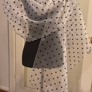 May include: A sheer white scarf with black polka dots is draped over a black dress form. A black bow is pinned to the shoulder. The scarf is lightweight and has a flowing design, suitable for formal wear.