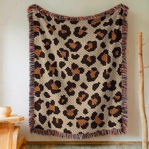 May include: A crocheted throw blanket with a leopard print pattern. The blanket has a fringe border in a variety of colors.