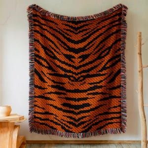 May include: A woven throw blanket with a tiger stripe pattern in orange and black. The blanket has a fringe border in a variety of colors.