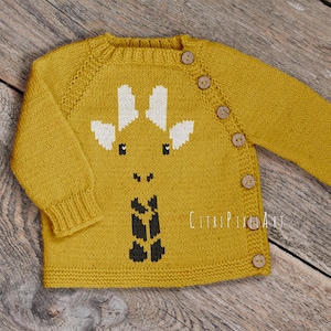 May include: A mustard yellow long-sleeved knit sweater featuring a white and black intarsia giraffe face design on the front. The garment has a ribbed crew neckline, cuffs, and hem, with a diagonal row of seven light brown wooden buttons.