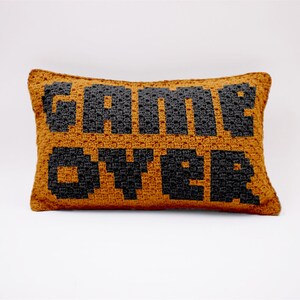 May include: A brown crocheted cushion with the words "GAME OVER" in black.