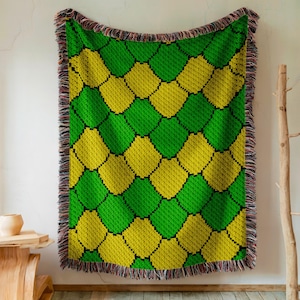 May include: A green and yellow woven throw blanket with a geometric pattern. The blanket has a fringe border.