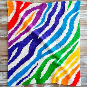 Peut inclure: Une couverture rectangulaire en crochet présentant un motif de rayures zébrées aux couleurs de l'arc-en-ciel. Le design se compose de rayures alternées rouges, orange, jaunes, vertes, bleues et violettes, entremêlées de rayures blanches.