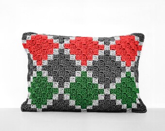 May include: A rectangular pillow with a geometric pattern in shades of red, green, gray, and white. The pillow is made of crocheted fabric.